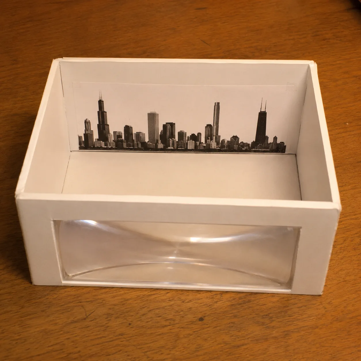 A simple enclosed apparatus — a Fresnel lens window mounted in the front of a foam-core box — used to demonstrate atmospheric-style refraction of a distant skyline.