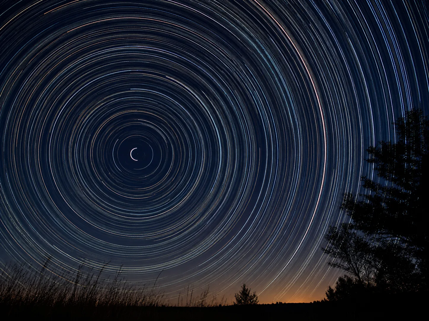A long-exposure photograph of the night sky showing perfect concentric circles of star trails turning around the fixed point of Polaris.